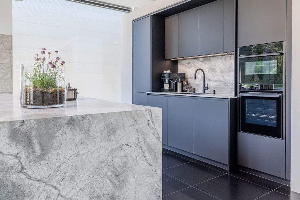 Küche mit dunklen Fronten, Natursteininsel und integrierten Geräten